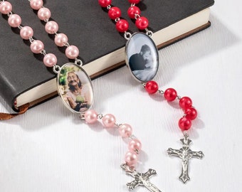 May include: Two pearl rosaries with silver crosses and oval photo charms. One rosary has pink pearls and a photo of an older woman, the other has red pearls and a photo of a person.