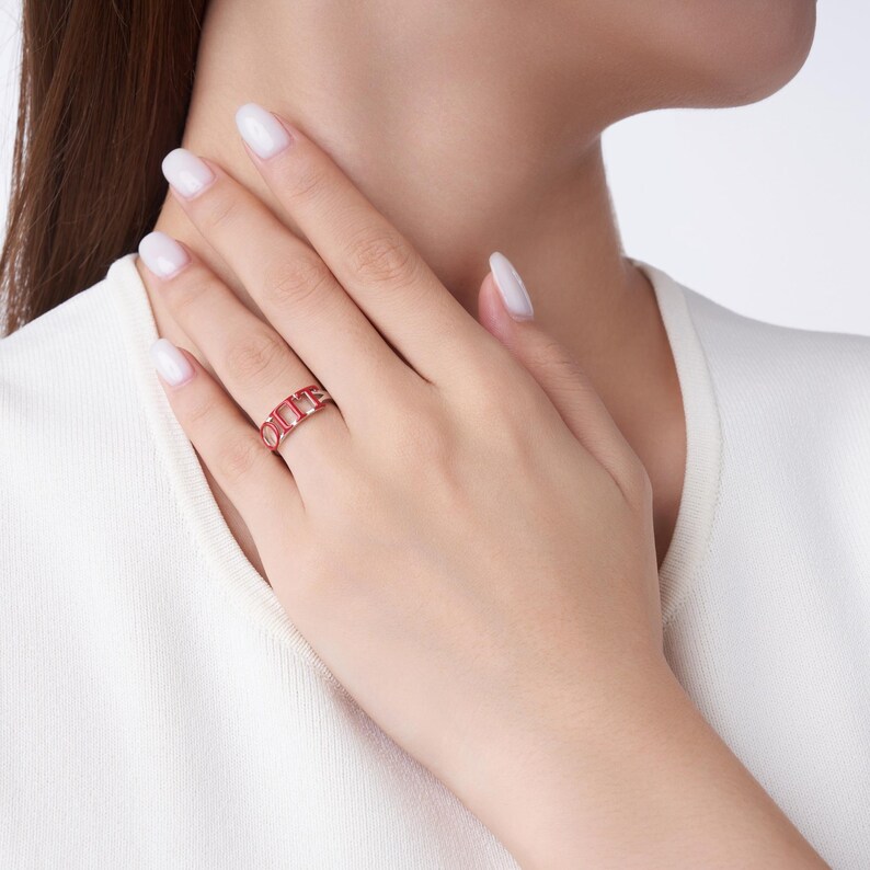 May include: A red ring with a rectangular design is worn on a finger. The ring has a series of connected rectangular shapes. The ring is made of a red material and is set against a white background.