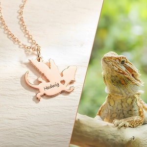 Pode incluir: Colar de ouro rosa com um pingente de dragão. O pingente é gravado com o nome "Hedwig".