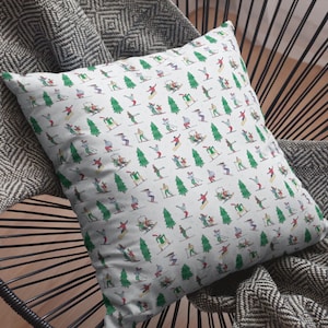 Puede incluir: Una almohada blanca con un patrón repetido de esquiadores y snowboarders en varias poses, junto con pinos verdes. La almohada está sentada en una silla con estampado blanco y negro.