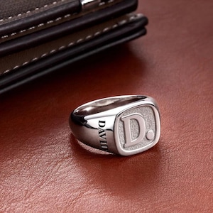 Può includere: Un anello a sigillo d'argento con una lettera "D" in rilievo e la parola "DAVID" incisa sulla fascia.