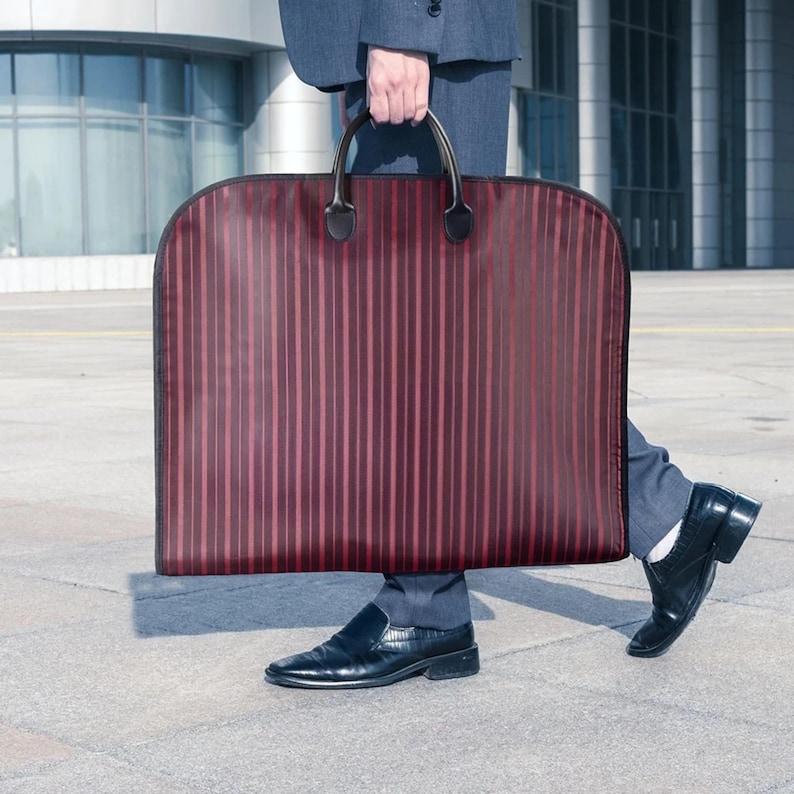 Puede incluir: Una funda de ropa burdeos con rayas verticales es llevada por una persona con traje. La bolsa tiene asas y ribetes negros. La persona lleva zapatos de cuero negros.