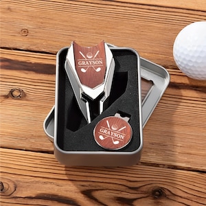 May include: A silver golf ball marker and a silver golf ball retriever with a woodgrain design. The marker and retriever are engraved with the name "GRAYSON" and a golf ball and crossed golf clubs. The items are in a silver gift box.