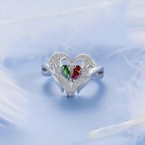 Puede incluir: Un anillo de plata con un dise&ntilde;o en forma de coraz&oacute;n. El anillo presenta dos piedras preciosas en forma de pera, una verde y otra roja, colocadas una al lado de la otra. El coraz&oacute;n est&aacute; adornado con peque&ntilde;as piedras brillantes.