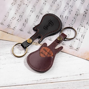 Op de afbeelding: Twee leren sleutelhangers in de vorm van een gitaar. Eén is zwart met de naam "Geoff" erop gegraveerd. De andere is bruin met een houten hartje waarop "When words fail me" staat.