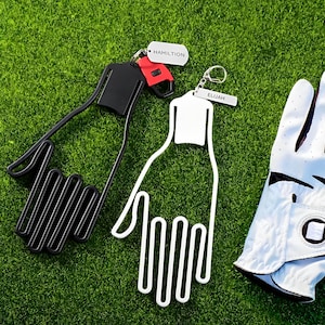 May include: Two golf glove holders, one black and one white, with the names "Hamilton" and "Elijah" on them. The holders are on a green grass background.