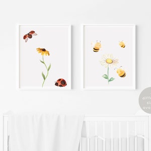 May include: Two framed watercolour prints. One shows a ladybug and a yellow flower, the other depicts bees and a daisy. The prints are displayed above a white cot. The text '4 different sizes available' is visible.
