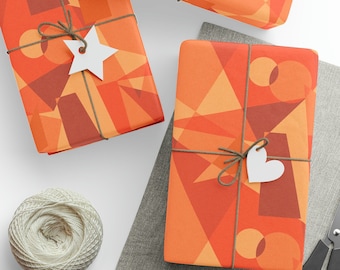 Può includere: Tre scatole regalo avvolte in carta con motivo geometrico arancione e rosso con spago bianco ed etichette. Le scatole sono su una superficie grigia.