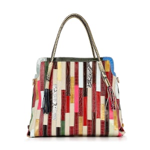 May include: A colorful patchwork handbag with a rectangular shape. The bag features vertical strips of various textures and colors, including red, pink, white, and brown. It has two handles with a gold chain design and decorative tassels.
