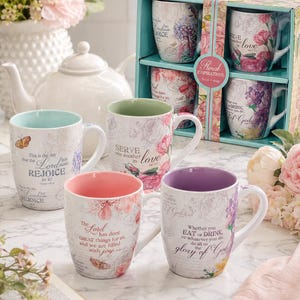 May include: A set of floral-themed mugs with inspirational quotes. The mugs feature pastel colors, floral designs, and text. One mug has a butterfly graphic. The set includes a gift box with four mugs. The mugs are white with various interior colors.