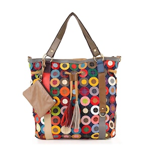 May include: A colorful tote bag with a unique design. The bag features a pattern of multi-colored circles on a dark blue background. It has brown straps, a small attached pouch, and decorative tassels. The bag is designed for carrying items.