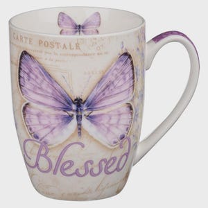 May include: White ceramic mug with a large purple butterfly design and the word "Blessed" in script. The mug also features a smaller butterfly and vintage postcard details. The handle has a purple accent.