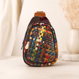 May include: A small sling backpack featuring a multi-colored woven leather front panel with a grid pattern of red, blue, green, yellow, and brown squares. The bag has a solid brown leather top handle, dark brown side panels, and a zipper closure.