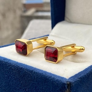 May include: A pair of gold cufflinks with red gemstone accents. The cufflinks are displayed in a blue velvet box.