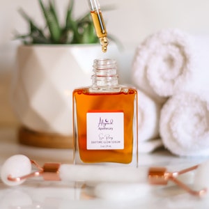 May include: A clear glass bottle with a dropper filled with a golden liquid. The bottle is labeled "Aligned Apothecary Sun Body Daytime Glow Serum 1 oz | 29 mL".