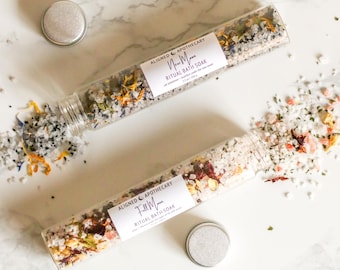 May include: Two glass tubes filled with bath salts and dried flowers. The tubes are labelled "New Moon Ritual Bath Soak" and "Full Moon Ritual Bath Soak".