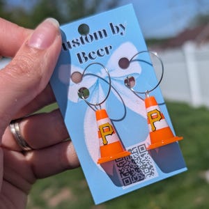 May include: A pair of hoop earrings featuring miniature orange and white traffic cone charms with a yellow letter P printed on each. The earrings are attached to a light blue display card with the text Custom by Beer and a QR code.