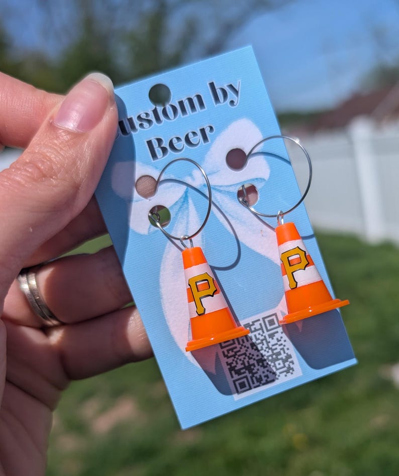 May include: A pair of hoop earrings featuring miniature orange and white traffic cone charms with a yellow letter P printed on each. The earrings are attached to a light blue display card with the text Custom by Beer and a QR code.