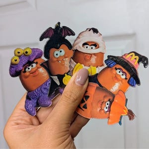 May include: A collection of vintage McDonald's Halloween-themed McNugget Buddies. The figures are in the shape of McNuggets, dressed as a vampire, mummy, witch, pumpkin, and a creature with purple hair and eyes.