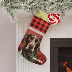 May include: A red and black plaid Christmas stocking with a brown and white dog wearing a green and red scarf. The stocking has the name "MURPHY" written on it.