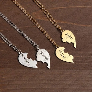 May include: Three gold and silver necklaces with heart-shaped pendants that are puzzle pieces. The pendants are engraved with the names "John", "Alice", and "Sietta & Vivienne".