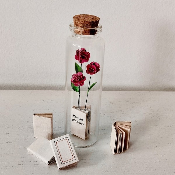 Fleurs et livre miniatures en papier dans une petite fiole en verre