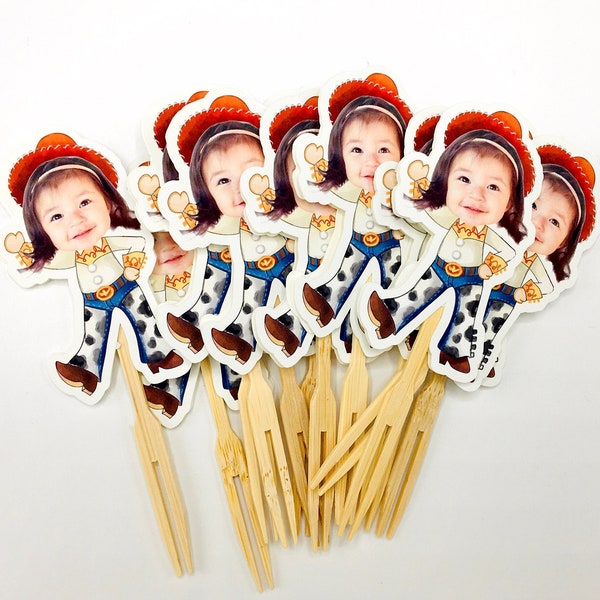 Op de afbeelding: Een set van acht cupcake-toppers met een cartoonafbeelding van een kind dat een cowboyhoed en outfit draagt. De toppers zijn gedrukt op wit karton en bevestigd aan houten spiesjes.