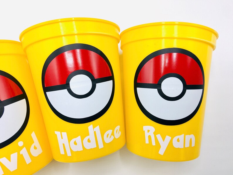 Pu&ograve; includere: Tre bicchieri di plastica gialli con un design Pokeball rosso, bianco e nero. I bicchieri hanno i nomi "David", "Hadlee" e "Ryan" stampati su di essi.