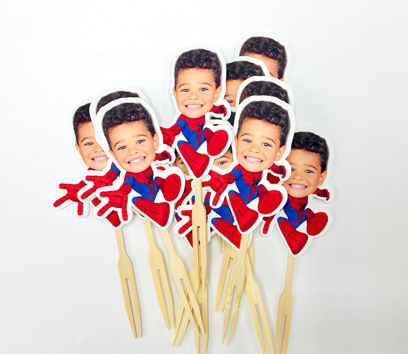 Puede incluir: Un conjunto de 8 adornos para cupcakes con la cara de un ni&ntilde;o con un disfraz de Spiderman. Los adornos est&aacute;n impresos en cartulina blanca y unidos a brochetas de madera.