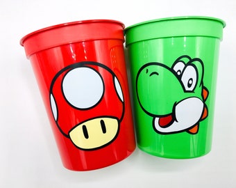 May include: Two plastic cups with cartoon characters. The red cup has a red and white mushroom with a yellow face. The green cup has a green Yoshi character with a red tongue.
