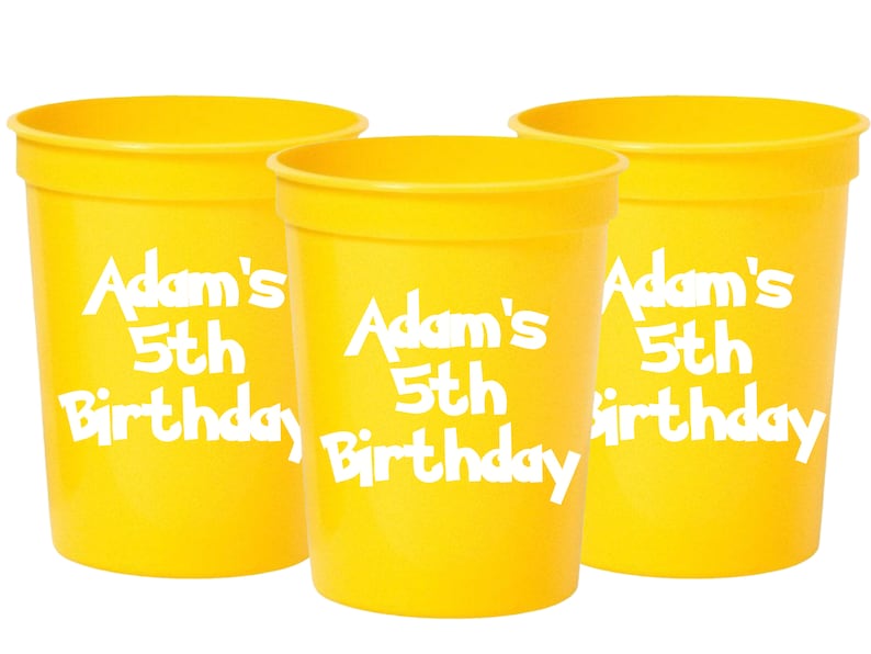 Pu&ograve; includere: Tre bicchieri di plastica gialli con testo bianco che dice "Adam's 5th Birthday".