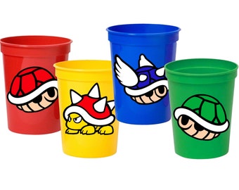 May include: Four plastic cups with different colored backgrounds and images of a Koopa Troopa from the Super Mario Bros. video game series. The cups are red, yellow, blue, and green.