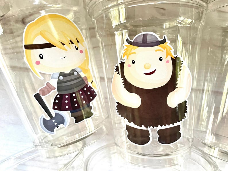 May include: Two clear plastic cups with colorful cartoon stickers. One sticker features a blonde girl with a braid, wearing a striped shirt and a polka dot skirt, holding an axe. The other sticker features a blonde boy with a beard, wearing a brown tunic and a horned helmet.