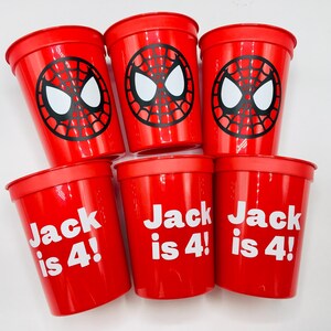 Puede incluir: Seis vasos de pl&aacute;stico rojos con un dise&ntilde;o de Spider-Man. Tres vasos tienen el texto "Jack is 4!" impreso en blanco.
