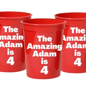 Puede incluir: Tres vasos de pl&aacute;stico rojos con el texto "The Amazing Adam is 4" impreso en ellos.