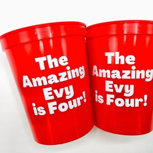 Puede incluir: Dos vasos de pl&aacute;stico rojos con texto blanco que dice "The Amazing Evy is Four!"