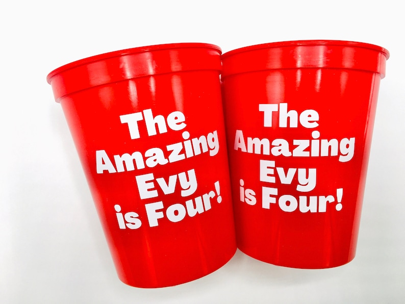 Puede incluir: Dos vasos de pl&aacute;stico rojos con texto blanco que dice "The Amazing Evy is Four!"