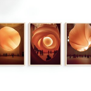 May include: Three framed photographs of large, orange, fabric sculptures hanging in a white room. The sculptures are suspended from the ceiling and appear to be made of a soft, flowing material. People are visible in the background, walking around the sculptures.