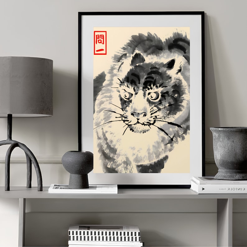 Op de afbeelding: Ingelijste kunstdruk met een tijgerillustratie in sumi-e-stijl. Het kunstwerk is voornamelijk zwart-wit met een beige achtergrond. Een rood Japans karakter staat in de linkerbovenhoek. Het gezicht van de tijger is het middelpunt.