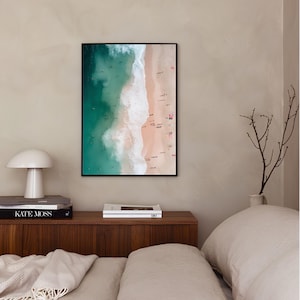 May include: An aerial photograph of a beach with turquoise water and white waves crashing on the shore. The sand is a light pink color and there are many people swimming and sunbathing.