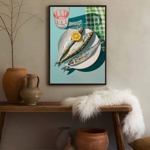 May include: A framed print of a still life featuring three whole sardines on a white plate with a lemon wedge. The plate is on a blue background with a green and white checkered tablecloth in the background.