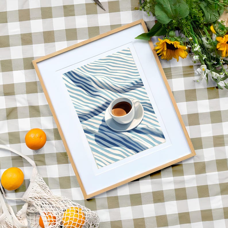 May include: A framed print of a cup of coffee on a blue and white striped fabric. The fabric is folded and the cup is in the center of the image.