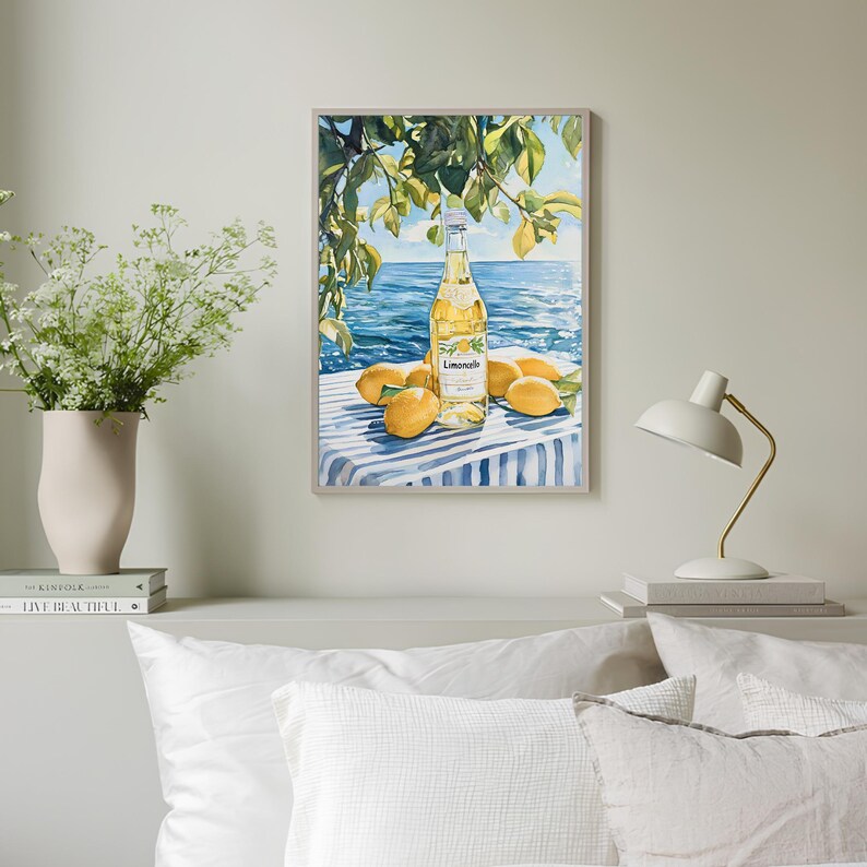 May include: A watercolor painting of a bottle of Limoncello on a blue and white striped tablecloth with lemons around it. The background is a blue ocean with green trees and a blue sky.