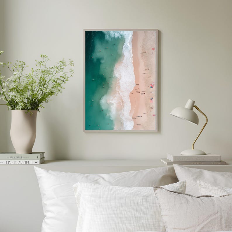 May include: An aerial photograph of a beach with turquoise water and white waves crashing on the shore. The sand is light pink and there are many people on the beach.