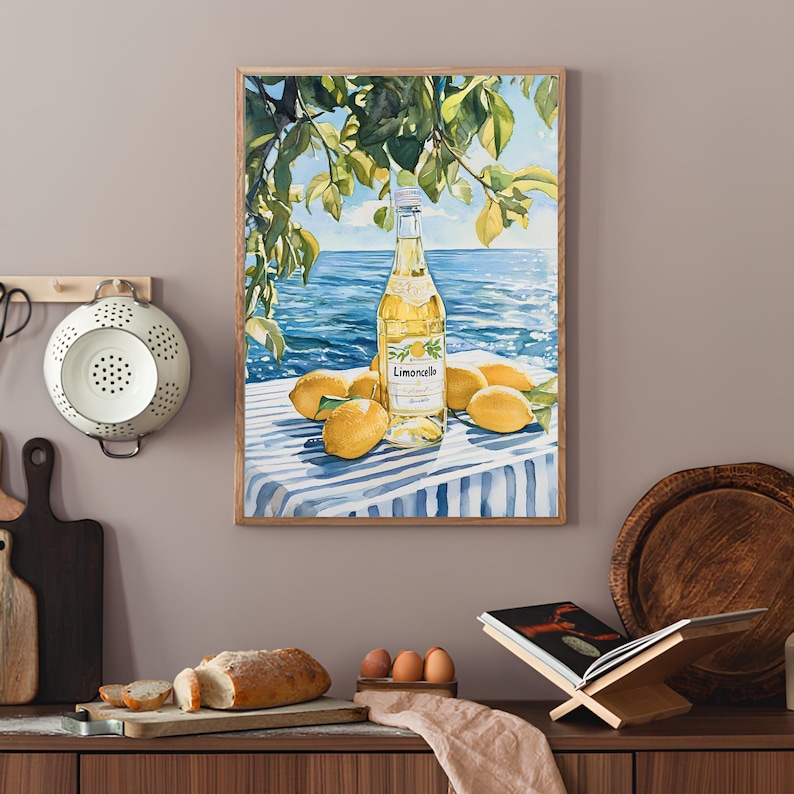 May include: A watercolor painting of a bottle of Limoncello liqueur with lemons on a blue and white striped tablecloth. The bottle is sitting on a table with a view of the ocean in the background.