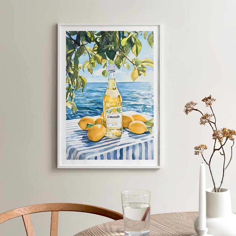 May include: A watercolor painting of a bottle of Limoncello on a blue and white striped tablecloth with lemons around it. The bottle is clear and has a yellow liquid inside. The background is a blue ocean with a green tree branch hanging over the scene.