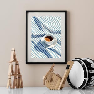 May include: A framed print of a white coffee cup with brown coffee on a blue and white striped fabric.