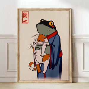 May include: A framed art print depicting a cartoon frog in a blue robe cradling a cat. The frog has yellow eyes and a black head. The cat is white and orange with a grumpy expression. Red Japanese text is in the upper left corner.