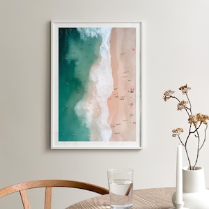 May include: An aerial photograph of a beach with turquoise water and white waves crashing on the shore. The sand is light pink and there are many people swimming and sunbathing.