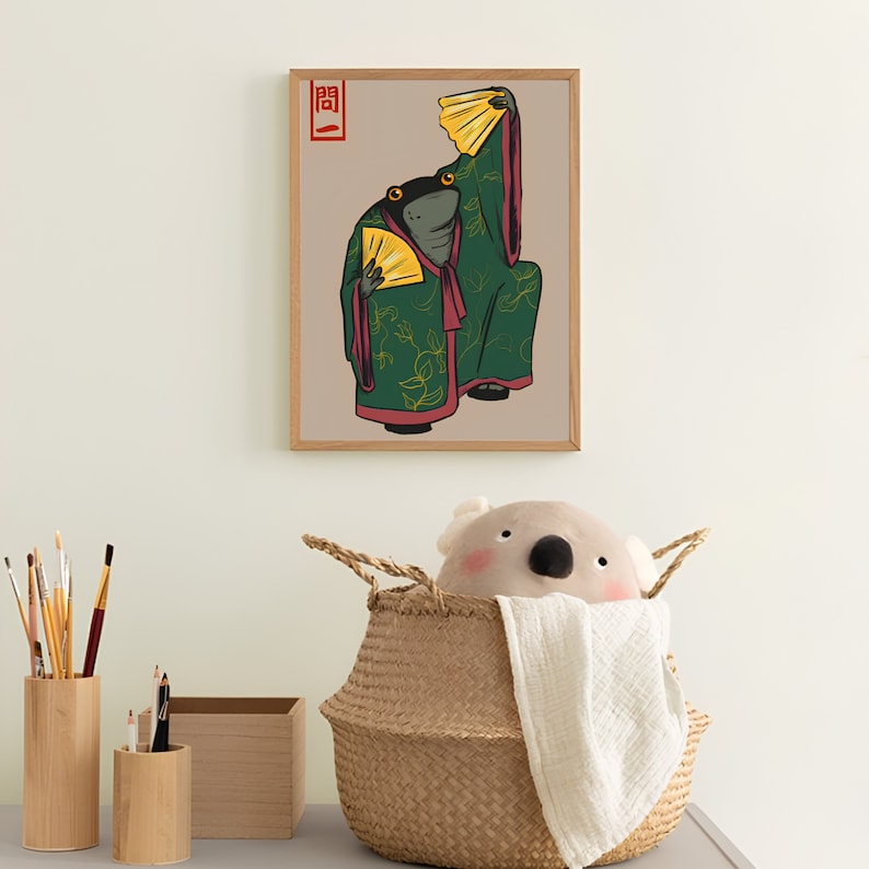 Op de afbeelding: Een ingelijste kunstprint met een gestileerde illustratie van twee kikkers in traditionele Japanse kledij, die gele waaiers vasthouden. De kikkers dragen groene gewaden met gouden bladmotieven en rode accenten. De print heeft een beige achtergrond en een houten lijst.